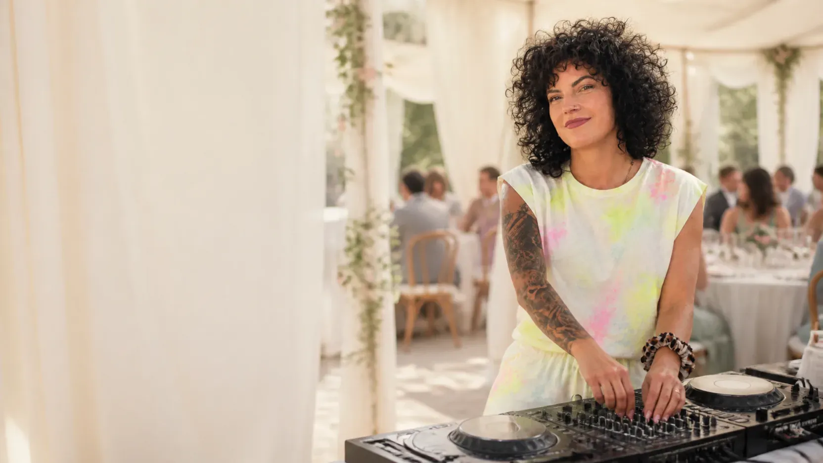 Janina Behrens am DJ-Pult in einem hellen Hochzeitszelt, im Hintergrund festlich gedeckte Tische